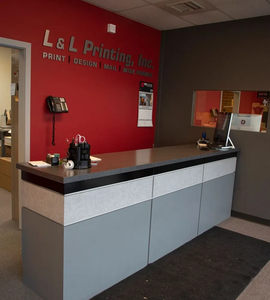 The front counter at L&L Printing, with the company name in silver letters on a red wall.
